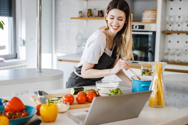 istock Young woman preparing lunch at home while looking at laptop 1389921407