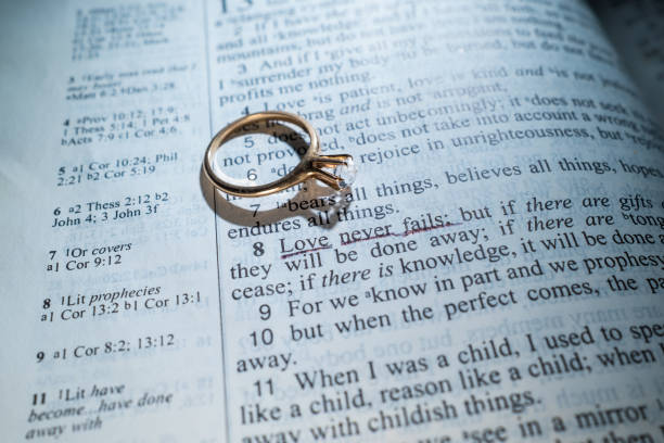 istock Woman's Gold Wedding Ring on a Bible with the Scripture Love Never Fails 1389922817
