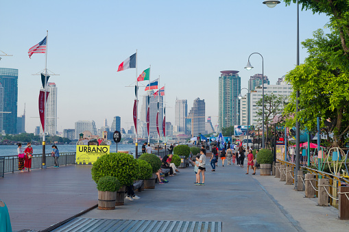 Sunset over promenade at Asiatique at Chao Praya river in Bangkok. View upstream river. People are walking on promenade with many flags. Asiatique is promenade area with restaurants in southern Bangkok