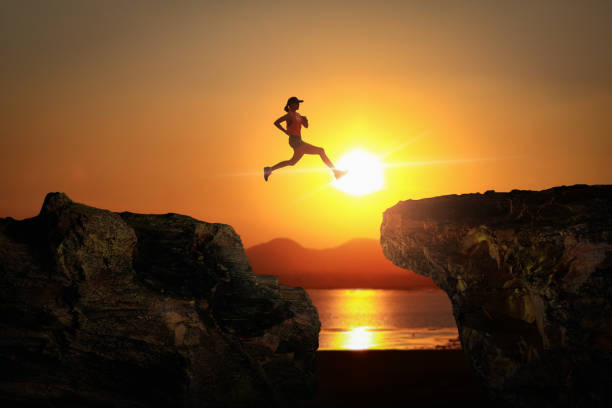 istock Silhouette of runner jumping over gap between cliff with evening sunset sky on background. 1389925808