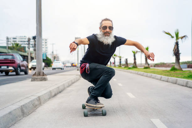 latin senior man skateboard en carril bici y divirtiéndose - monopatín actividades recreativas fotografías e imágenes de stock