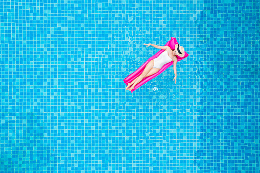 Top view of young asian woman in swimsuit on the pink air mattress in the swimming pool.