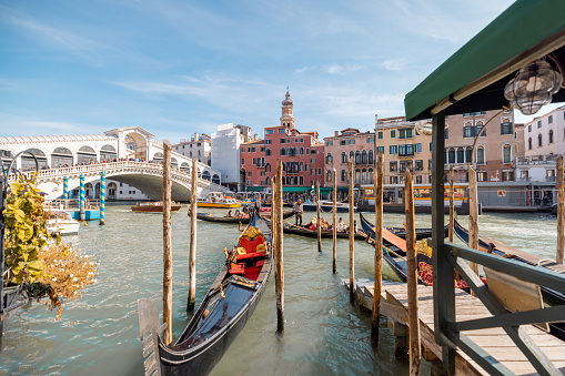 View on Grand Canal with famous Rialto bridge and gondolas in front in Venice. Italian landmarks and traveling Italy concept. Cityscape in autumn sunny day