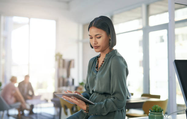 shot of a young businesswoman using a digital tablet in a modern office - using tablet imagens e fotografias de stock