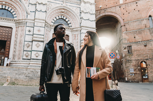 A young adult couple is walking in the city of Siena at sunset. They are on vacation together.
