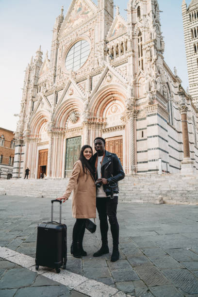 Portrait of two young adult people with a suitcase looking at camera Portrait of two young adult people with a suitcase looking at camera. They are standing near the Siena Cathedral. tourist site stock pictures, royalty-free photos & images