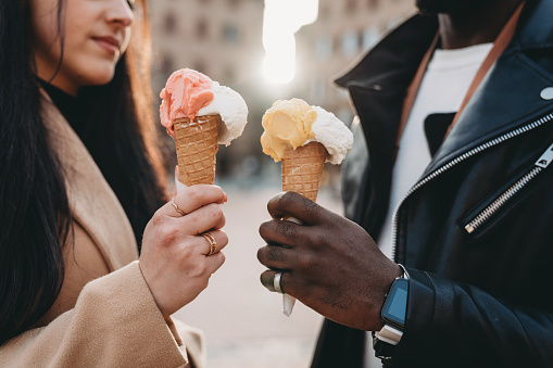 Close up shot of two people holding ice-creams at sunset. Close up on the hands holding the ice-creams.