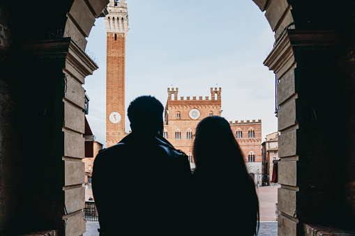 Rear view of a young couple admiring Piazza del Campo in Siena, Tuscany, Italy. People silhouette.