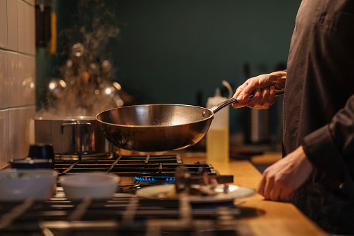 Man holding wok over gas stove and making dinner