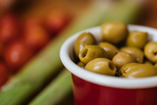 Cropped photo of olives in a small ceramic bowl with vegetables in background