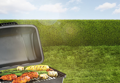 BBQ grill in a backyard with green grass and hedge fence