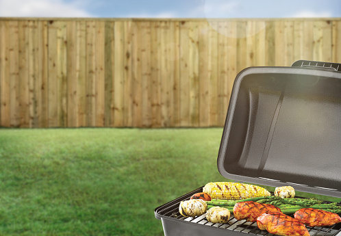 BBQ grill in a backyard with green grass and wood fence