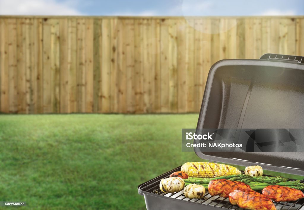 BBQ grill in a backyard with green grass and wood fence Barbecue Grill Stock Photo