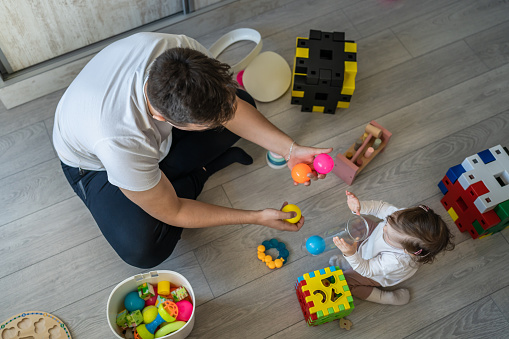 baby girl and her father young caucasian man with daughter playing at home happy sitting on the floor with toys in day fatherhood childhood family concept real people copy space top view