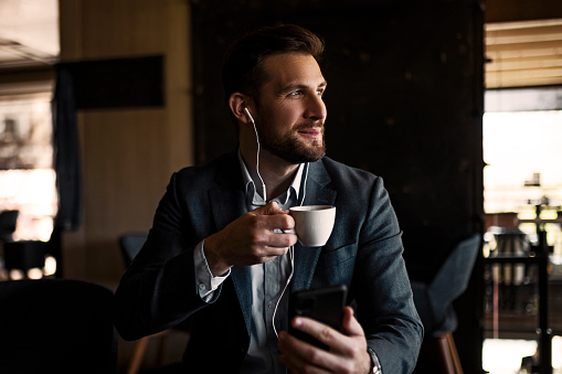 Young businessman in cafe using smart phone with headphones