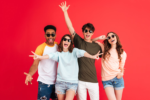 Portrait of a cheerful happy group of multiracial friends in summer clothes having fun while standing together isolated over red background