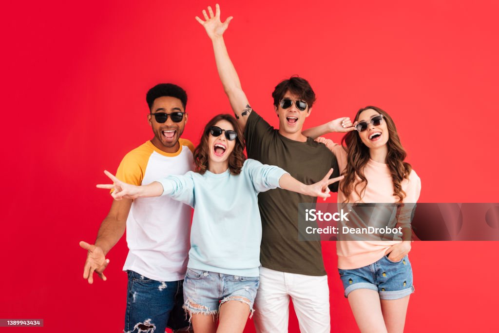 Portrait of a cheerful happy group of multiracial friends Portrait of a cheerful happy group of multiracial friends in summer clothes having fun while standing together isolated over red background Friendship Stock Photo