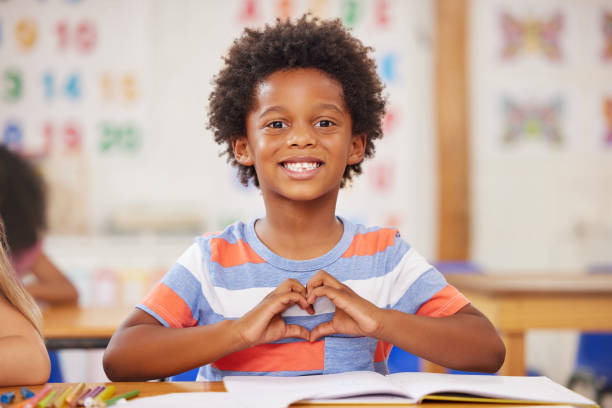 Shot of a preschool student forming a heart shape with his hands while sitting in class Preschool is where your child develops their own stand-out personality cute boy show love symbol hand stock pictures, royalty-free photos & images
