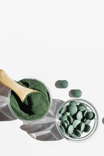 Photo of natural additives and superfood. green spirulina algae powder and pills in glass bowls on white background. healthy lifestyle concept. organic food