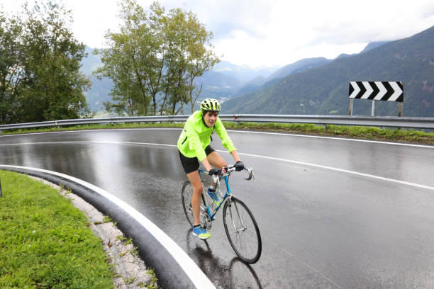 menino ciclista com bicicleta de corrida enquanto faz uma curva em estrada molhada durante o treinamento esportivo enquanto chove - pedal bicycle sports training cycling - fotografias e filmes do acervo