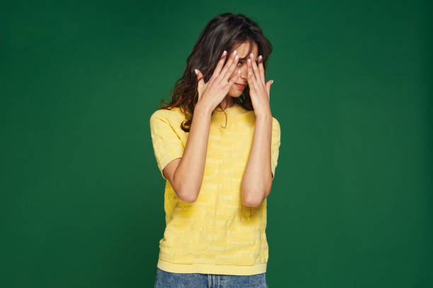 istock Scared or embarrassed young girl covering eyes by hands, peeping on green studio background with copy space 1389949669