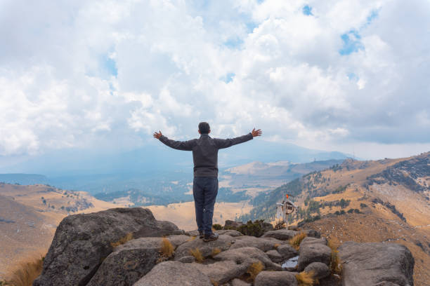 a man standing with open arms on the ledge of a mountain