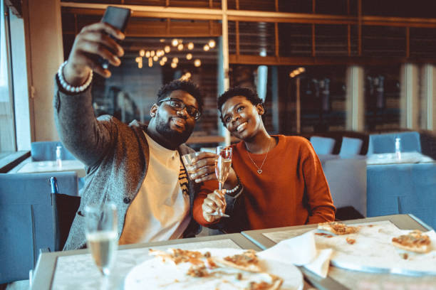 Friends gathering at the restaurant Friends gathered at the restaurant eating pizza and drinking some wine and spirit. At this photo they capturing a selfie photo while making a toast. black people eating stock pictures, royalty-free photos & images