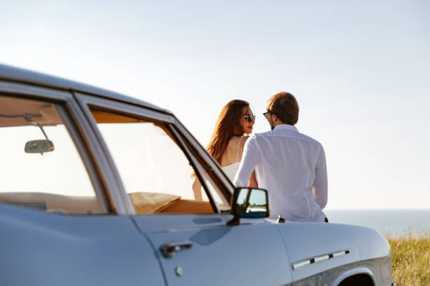 istock Beautiful young couple resting together outdoors while leaning on a car 1389953235