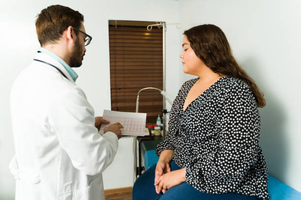 Female patient with heart problems Cardiologist showing and explaining the electrocardiogram results to an overweight young woman with heart problems fat mexican man pictures stock pictures, royalty-free photos & images