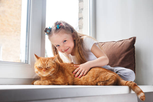 istock Cute child embraces with tenderness and love a red cat on window 1389959632