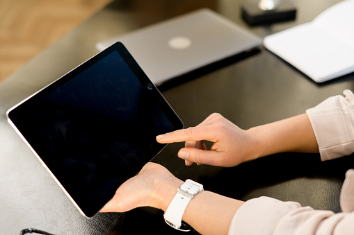 Back view at digital tablet with empty display in female hands, blank screen of gadget, tablet with blank monitor, mockup, copy space, businesswoman using new computer app