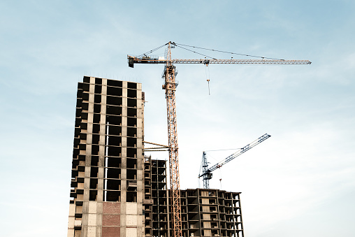 Construction site with frames of multistory buildings and cranes at blue white cloudy sky background