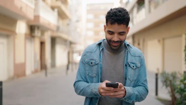 Young arab man using smartphone walking at street