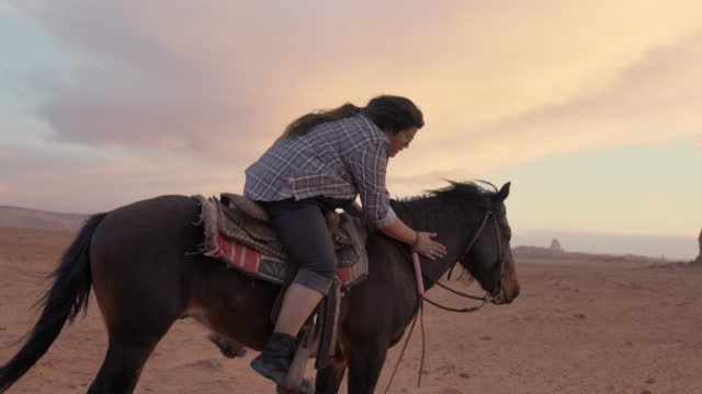 Young Navajo Girl Petting the Horse She is Riding on in Monument Valley Tribal Park in Arizona under a Beautiful Sunset