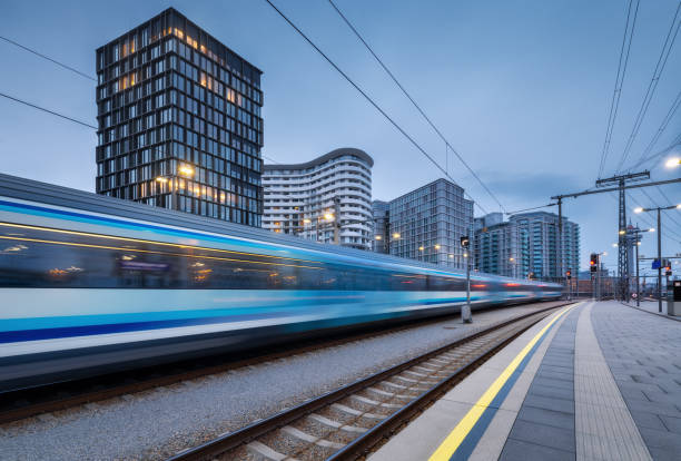 treno ad alta velocità in movimento sulla stazione ferroviaria al crepuscolo. spostamento blu moderno treno passeggeri intercity, piattaforma ferroviaria, edifici, luci della città. ferrovia a vienna, austria. trasporto ferroviario - stazione della metropolitana foto e immagini stock