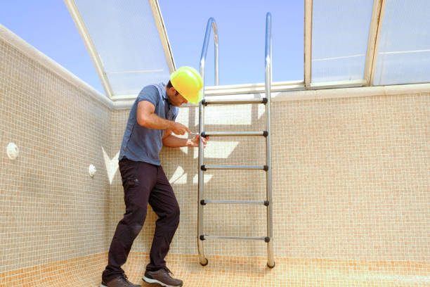 istock worker with hard hat and screwdriver installing a ladder in an empty swimming pool under construction. 1389966278
