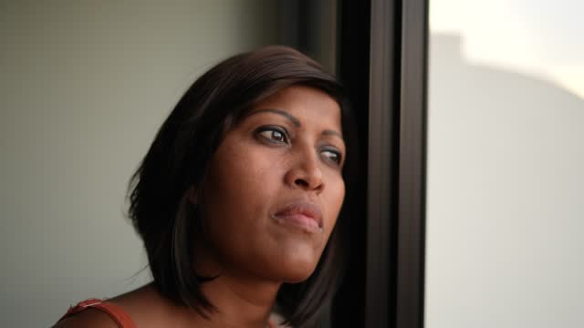 Contemplative woman looking through the window at home