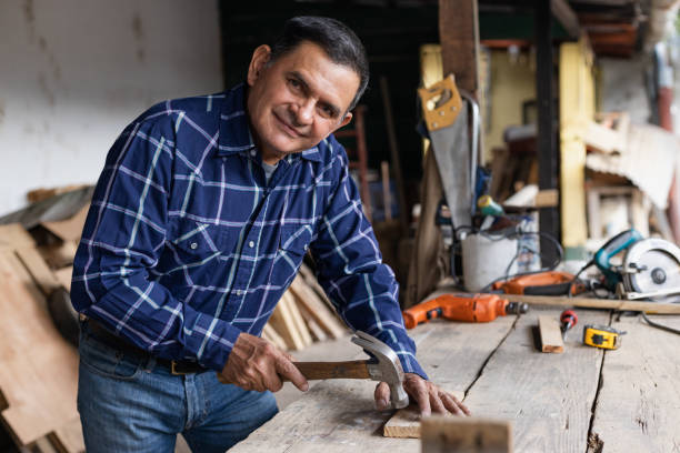 istock Hispanic carpenter nailing into wood - worker man with carpentry tools - man hammering 1389970287
