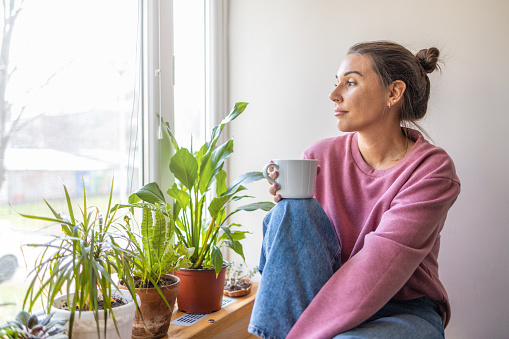 Young woman sitting by window, enjoying hot drink at home