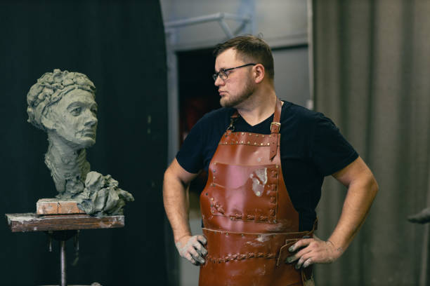 istock Man sculptor creates sculpt bust clay human woman sculpture. Statue craft creation workshop 1389975894