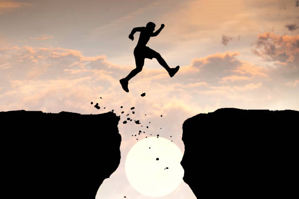istock Man Jumping Across a Gap between the Cliffs in the Mountains. 1389983201