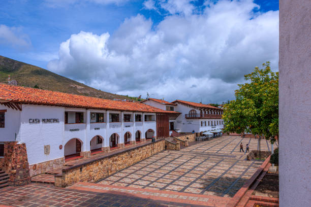Guatavita, Colombia - Looking at one side of one of the three main town squares of the Andes town of Guatavita in the Cundinamarca Department of the South American country of Colombia. A section of the Cordillera Oriental of the Andes Mountains can be seen in the background. Though completed in the 1960s, the town is designed and built in the colonial Spanish style of architecture. Situated about an hour's drive from the capital city of Bogotá, it is located at an elevation of 8,660 feet above sea level and is a popular weekend destination with both local Colombians, and tourists. Photo shot in the early afternoon sunlight; horizontal format. Copy space. una de las tres plazas principales de la ciudad de guatavita en la cordillera oriental de la cordillera de los andes en colombia. vista de un lado de la plaza, mirando a los edificios de oficinas municipales, bancos, restaurantes y hoteles. arquitectura de