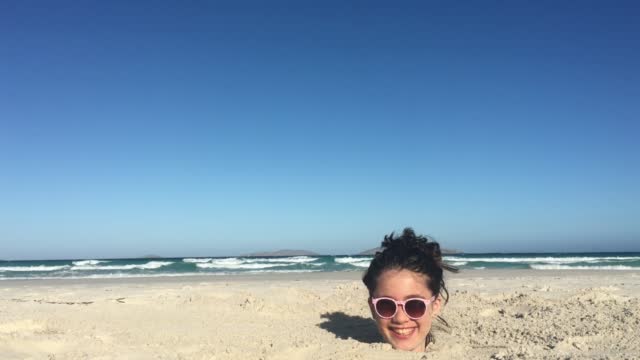 Young girl is buried up to her head in sand at the beach