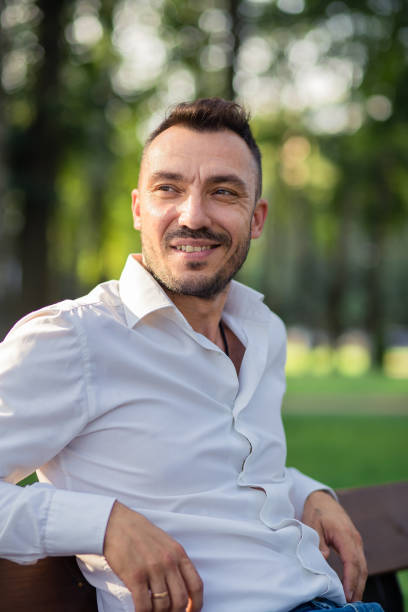 istock Smiling handsome man in a white shirt is resting sitting on a bench. 1389990263