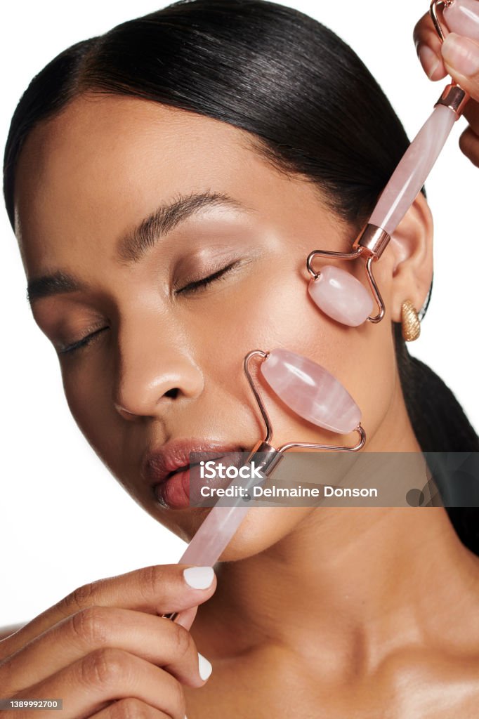 Studio shot of an attractive young woman using a jade roller on her face against a white background Roll those wrinkles right away Jade Roller Stock Photo