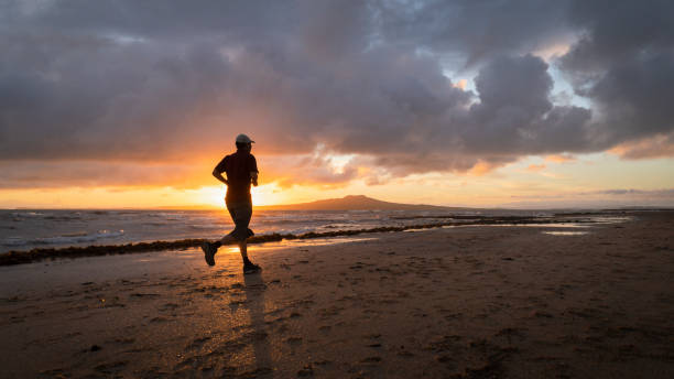 Silhouette man running on Takapuna beach at sunrise, Rangitoto Island in the background, Auckland. Silhouette man running on Takapuna beach at sunrise, Rangitoto Island in the background, Auckland. rangitoto island stock pictures, royalty-free photos & images