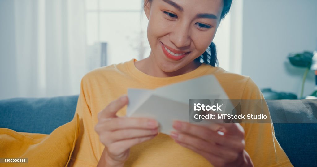 Young Asian woman feel excited unpacking gift box sitting on couch in living room at home. Young Asian woman feel excited unpacking gift box on couch in living room at home. Greeting Card Stock Photo