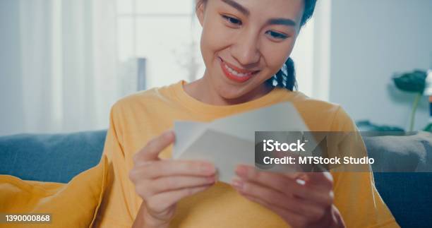 Young Asian Woman Feel Excited Unpacking Gift Box Sitting On Couch In Living Room At Home Stock Photo - Download Image Now