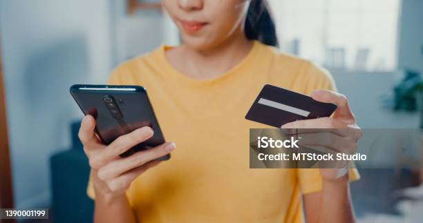 Close Up Of Young Asian Woman Holding Credit Card And Using Phone Making Payment Online Sitting At Desk In Living Room At Home Stock Photo - Download Image Now