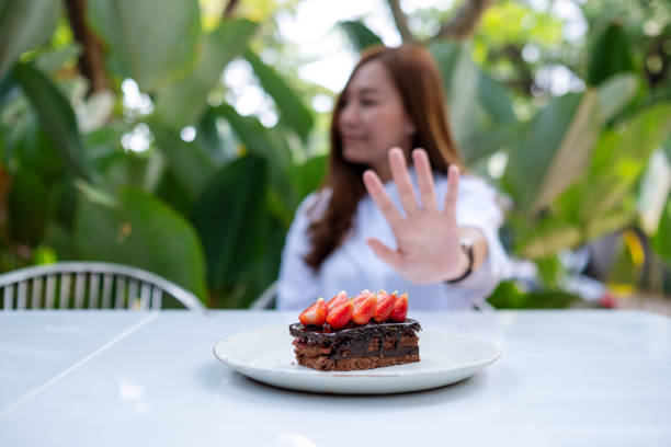 a young woman making hand sign to refuse a piece of strawberry chocolate cake - cake pick imagens e fotografias de stock